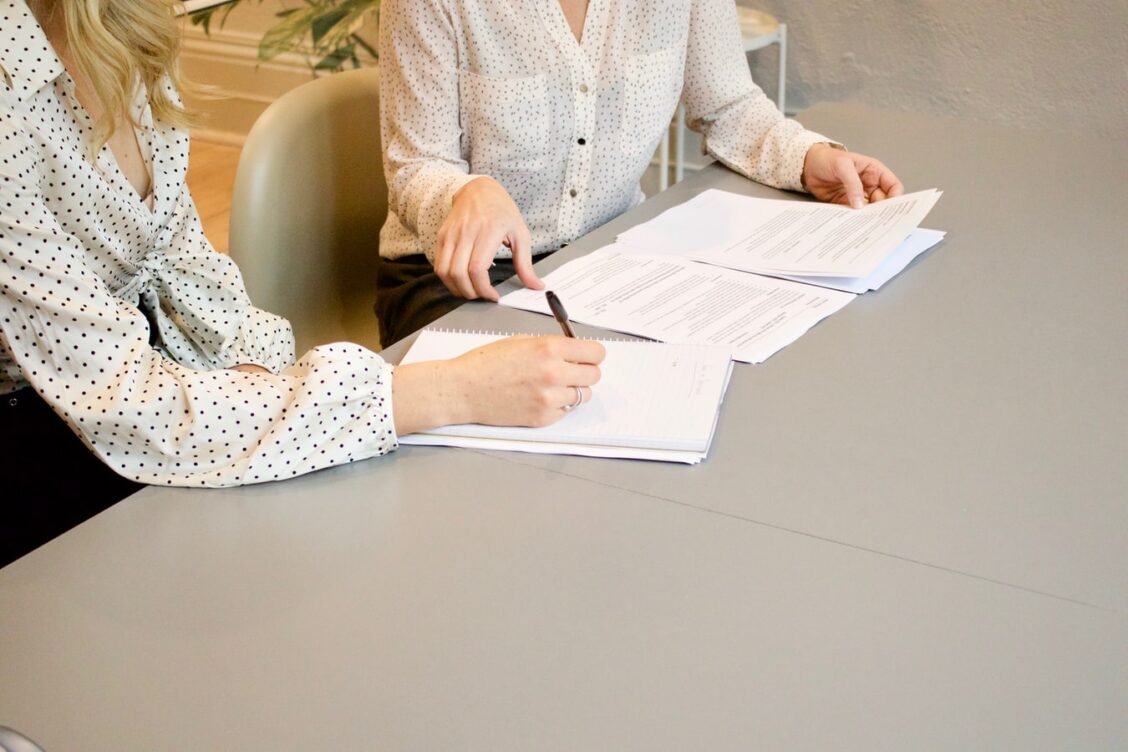 Two women sitting at a table with papers and pens.